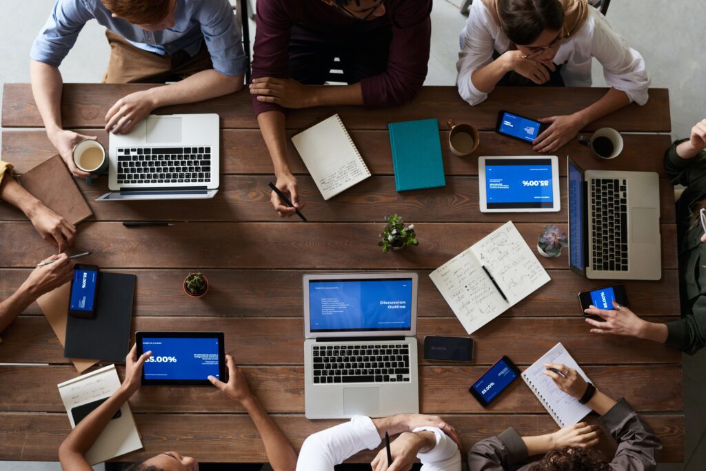 Top View Photo Of People Around Wooden Table with laptops and notepads discussing topics
