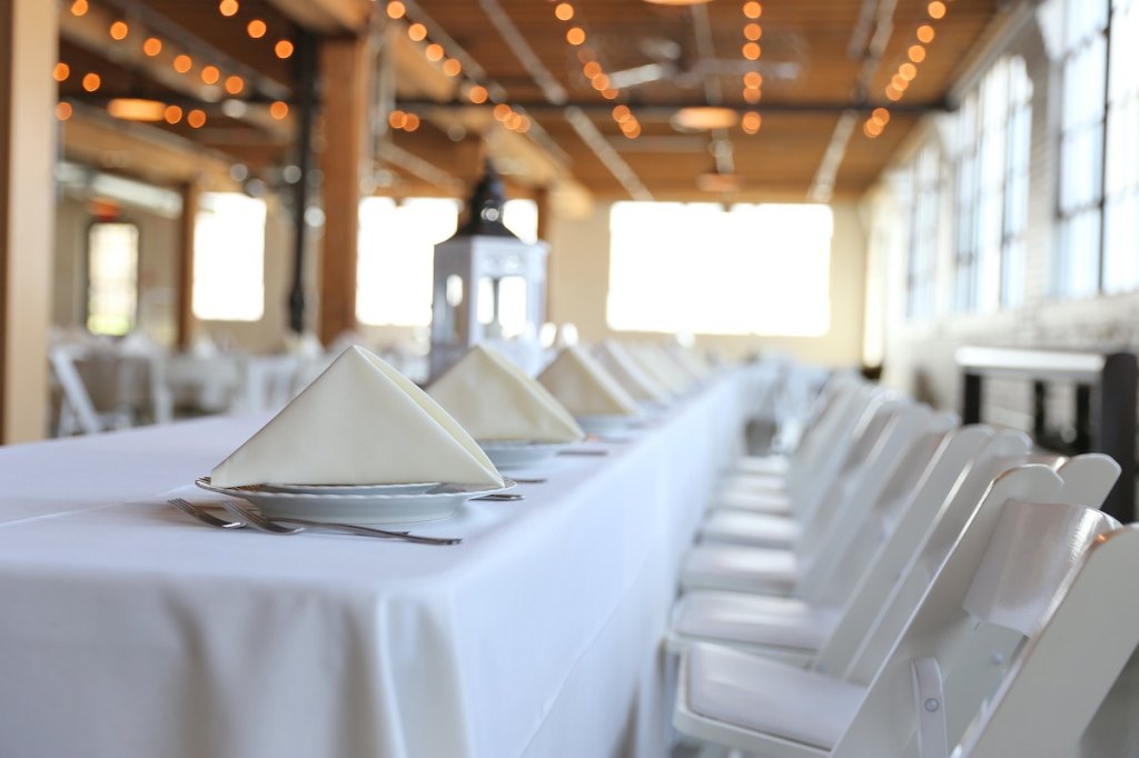 An interior shot of a dining hall at a business event venue, with a long table covered in a white tablecloth and set with white dinner ware.