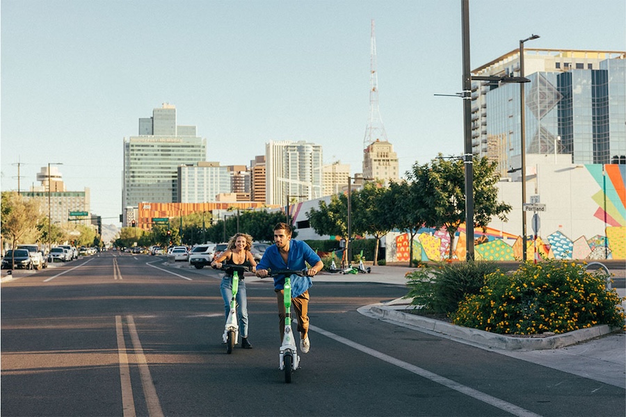 A man and a woman ride electric scooters in downtown Phoenix.