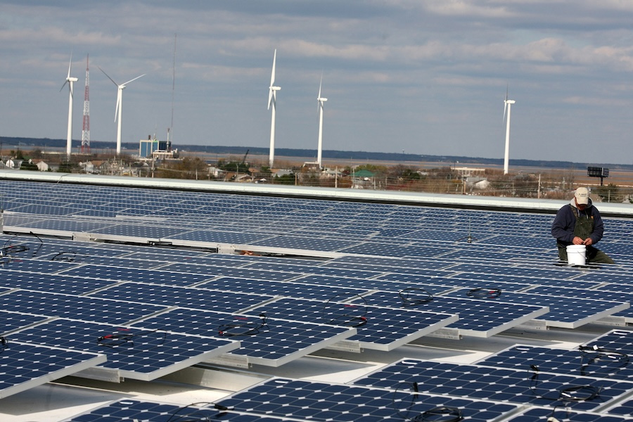 A view overlooking the rooftop solar array at the Atlantic City Convention Center, with windmills visible in the background and a maintenance person busy with repairs in the middle-ground.
