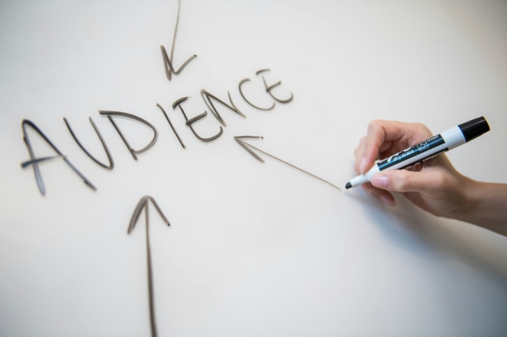 Woman's hand writing the word audience on a whiteboard with arrows