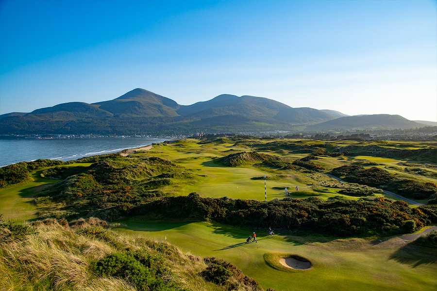 An overhead shot of a golf course in Northern Ireland with sweeping views of Mourne Mountains, characterized by rolling curves and green grass.