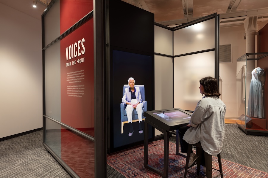In this interactive immersive experience, a woman sits across from a life-sized projection of an elderly woman recounting stories of her past experiences during WWII.