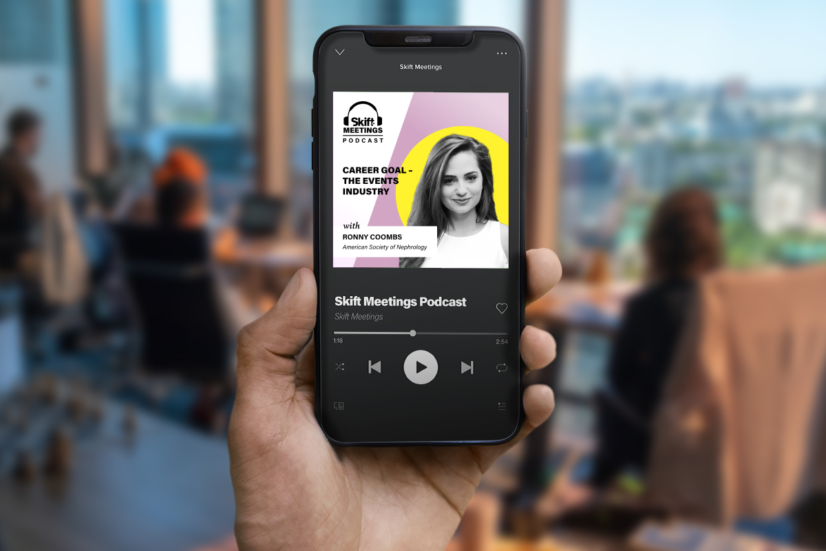 Person holding a phone up that is playing the Skift Meetings Podcast episode featuring Ronny Coombs, exhibits manager of the American Society of Nephrology (ASN).