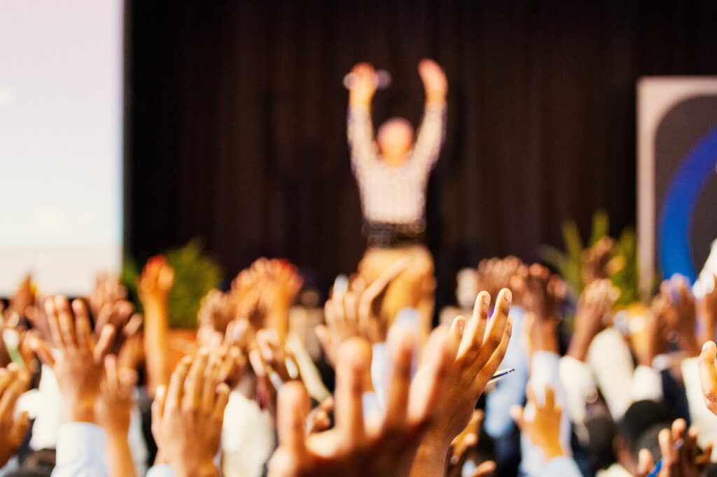 crowd playing interactive games at event by putting their hands up to match the speaker at the front of the crowd