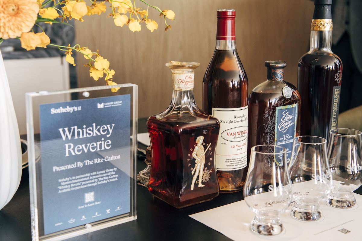 Four bottles of whiskey with corresponding tumblers and a blue sign with the words "Whiskey Reverie"