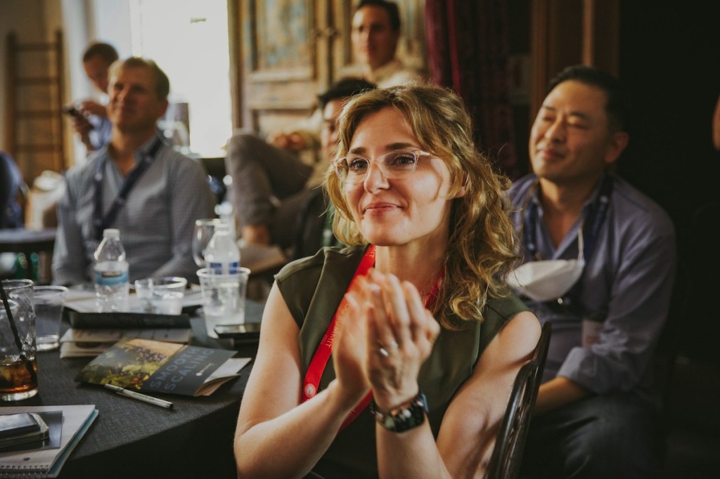 Female association executive sitting at a roundtable at a conference looking up toward the speaker and clapping