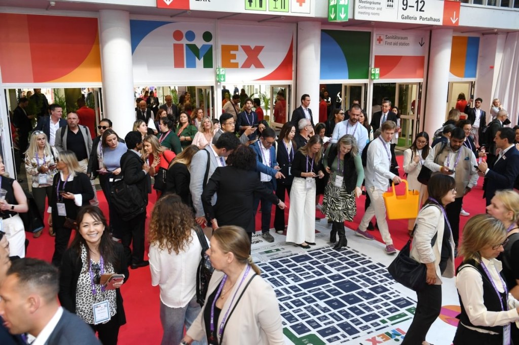 The entrance to the IMEX exhibition, busy with people looking down at a floor plan on the floor.