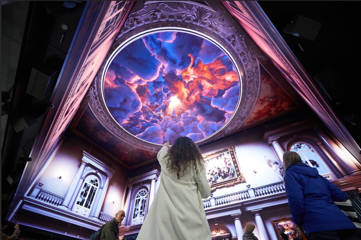 Person looking up and ponting at the ceiling which shows a large digital screen imitating the interior of a church.