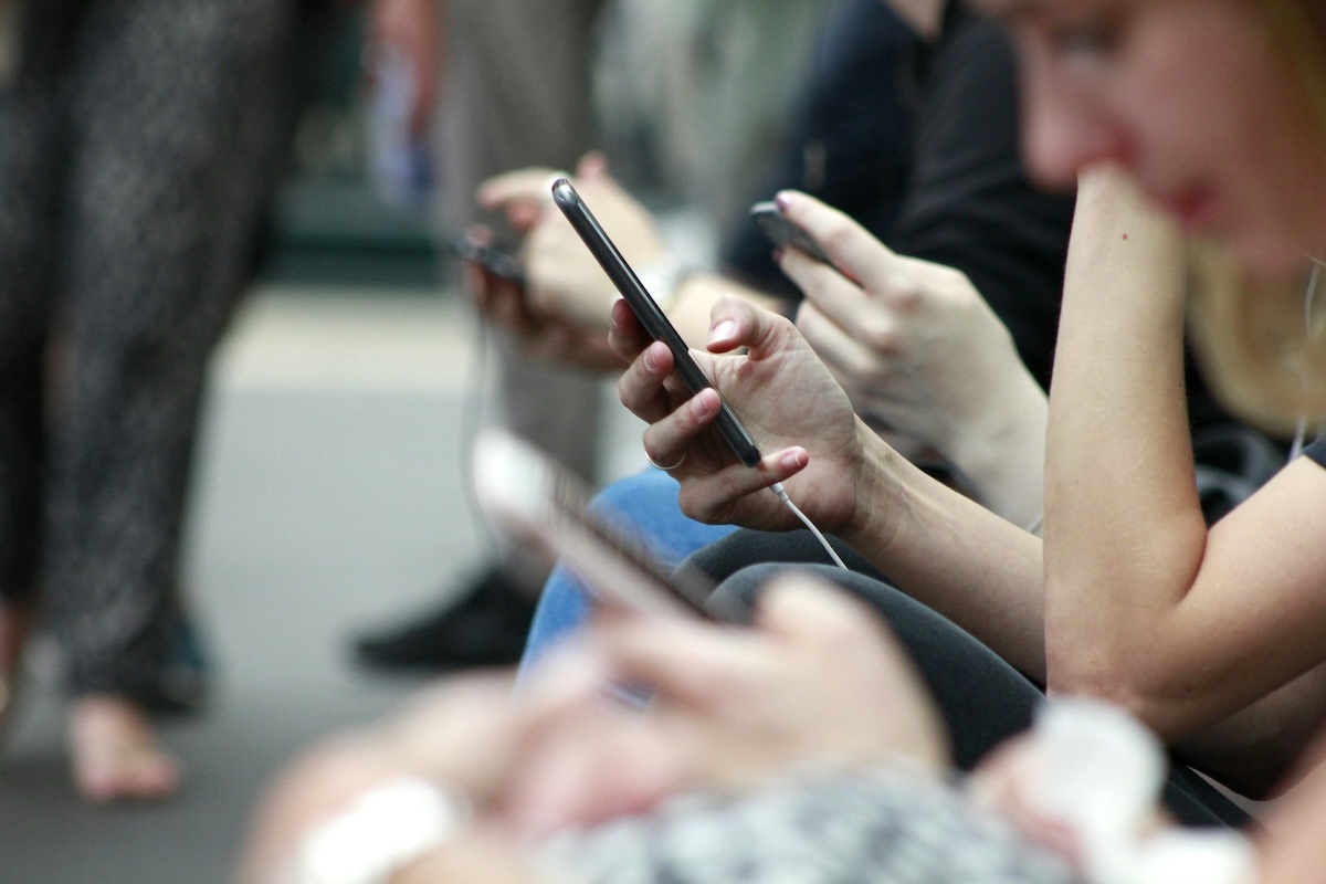 Person holding a smartphone at an event sitting in a row of chairs